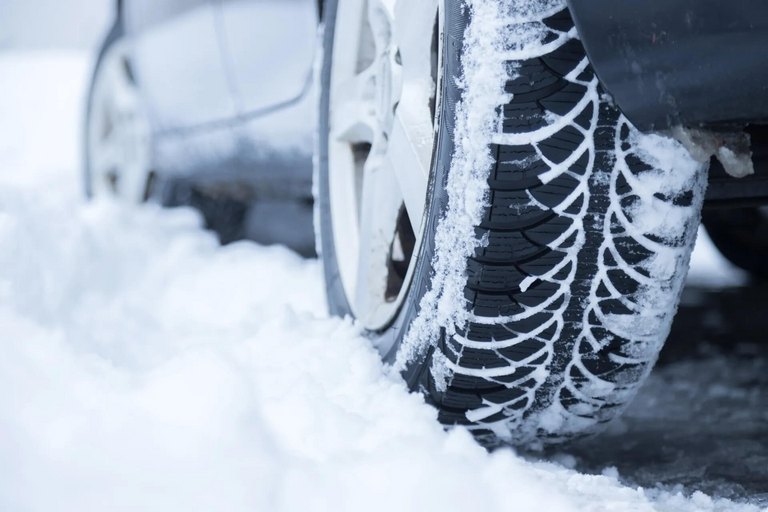 Nahaufnahme eines Autos mit Winterreifen auf schneebedeckter Straße, klar erkennbares Reifenprofil mit Schneeansatz – steht für sicheres Fahren im Winter und den professionellen Winterreifenservice in Piringsdorf.