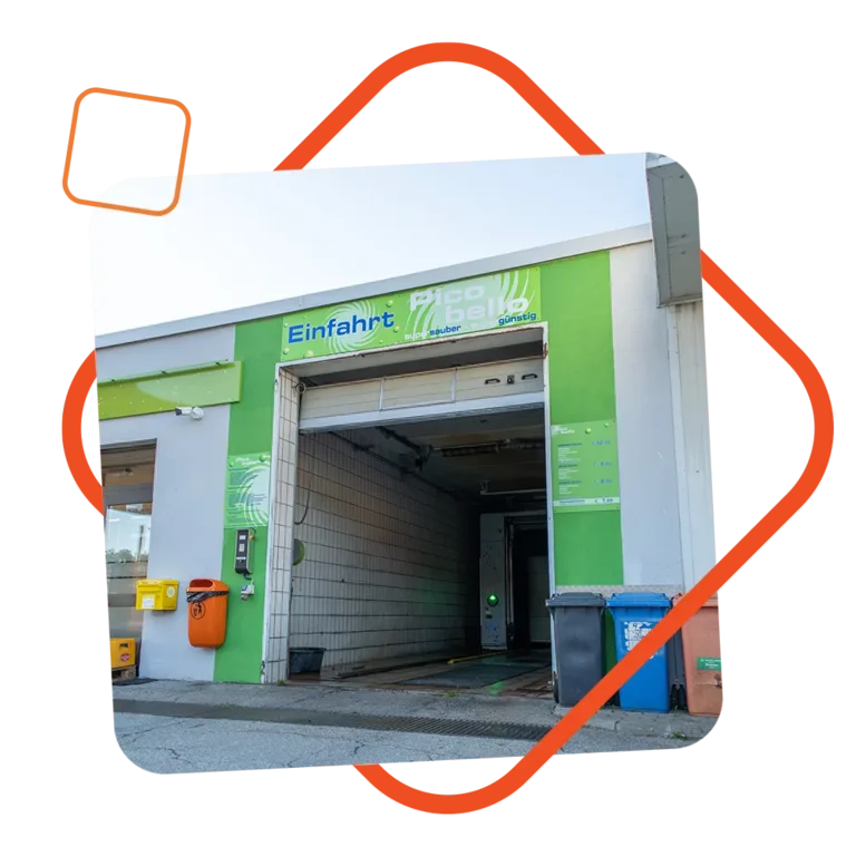 Einfahrt der Pico Bello Autowaschanlage bei der Tankstelle Loibl, mit grün-weißer Beschilderung, automatischem Rolltor und gut sichtbarem Preis- und Programmbereich; eingerahmt von einem orangefarbenen grafischen Element.