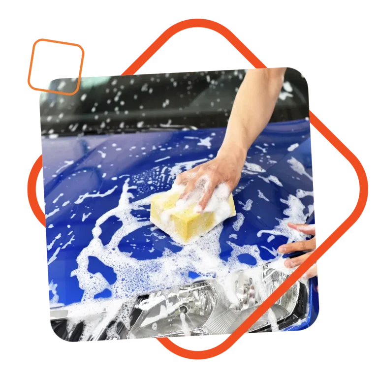 Hand mit Schwamm reinigt schaumige Motorhaube eines blauen Autos von Hand, eingerahmt von einem orangenen grafischen Element – steht für persönliche Autopflege und individuelle Beratung.